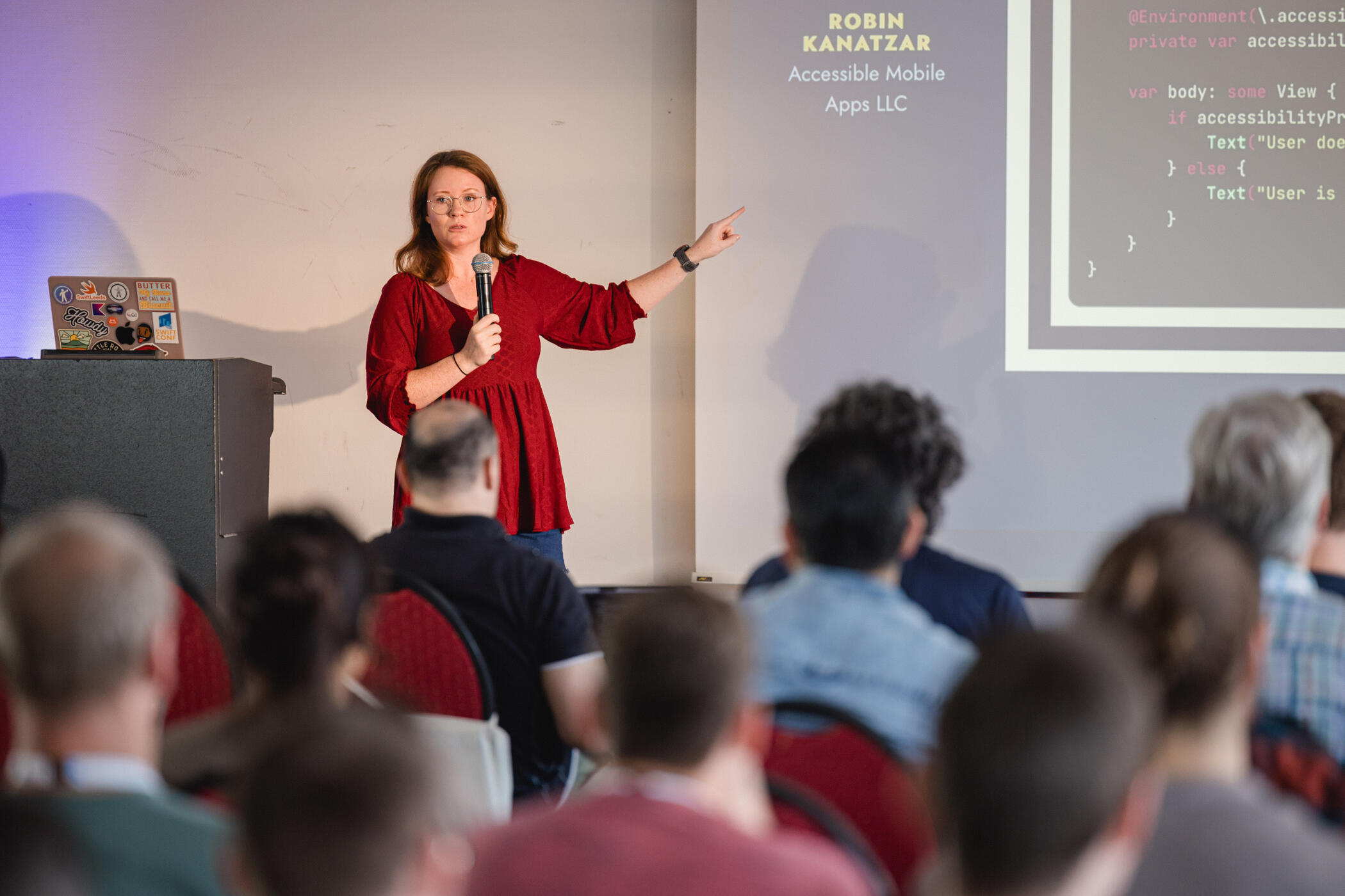 Photo of Robin giving a presentation pointing to a slide with code, with a microphone in her hand